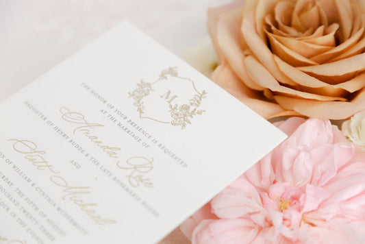Close-up detail of Amanda Rose Suite elegant wedding invitation card with floral monogram and pink roses in the background.