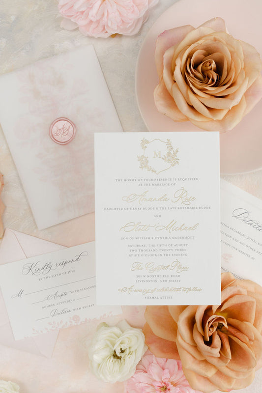 Elegant wedding invitation of the Amanda Rose suite with gold foil details, dark gray ink, and ivory cardstock, displayed with etched roses on vellum and a wax seal stamp.