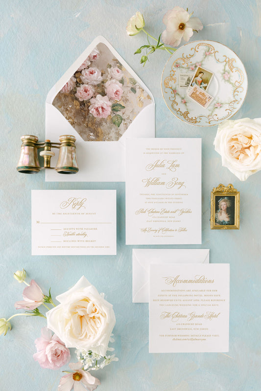 An invitation suite laid out with gold foil details on ivory cardstock, surrounded by floral elements and an envelope with a floral liner.
